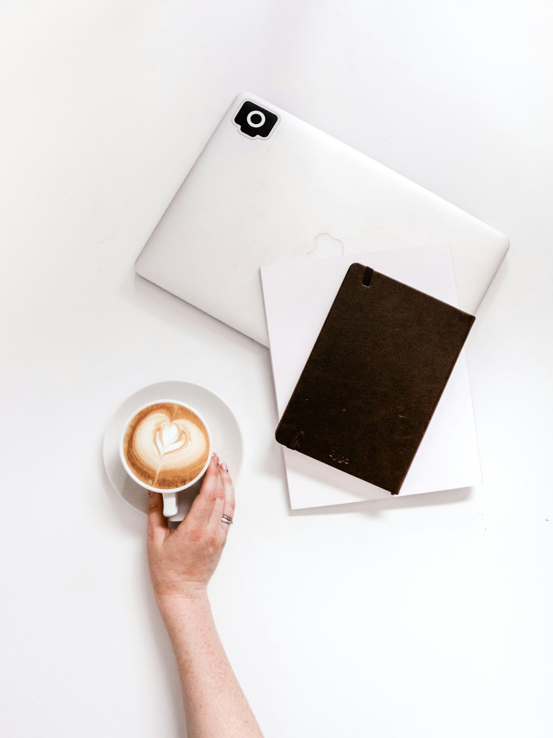 Overhead view of hands writing research notes beside a laptop and coffee cup